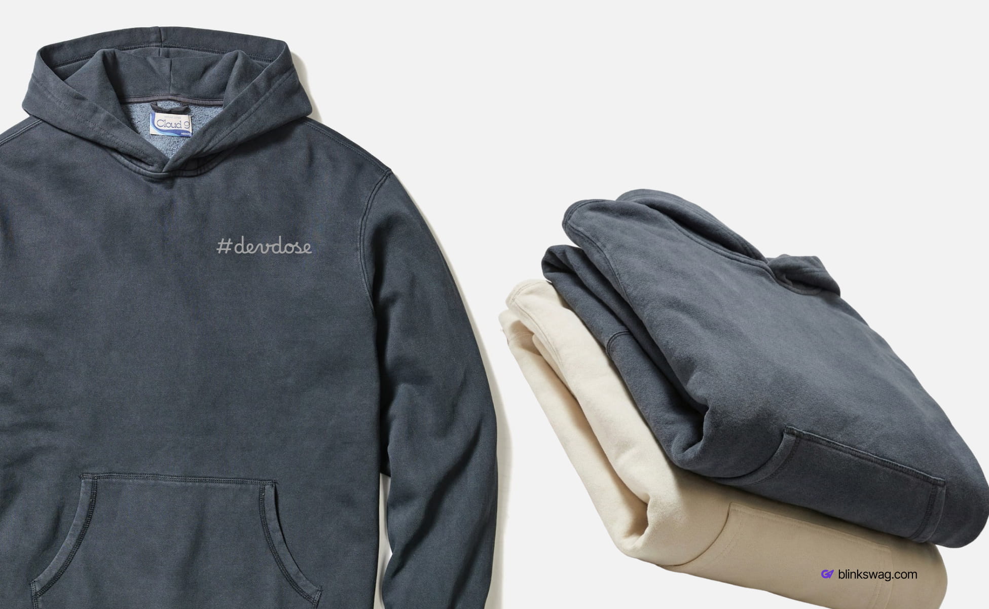 Dark grey Marine layer fleece hoodie embroidered with "#devdose" displayed alongside folded cream and grey hoodies.